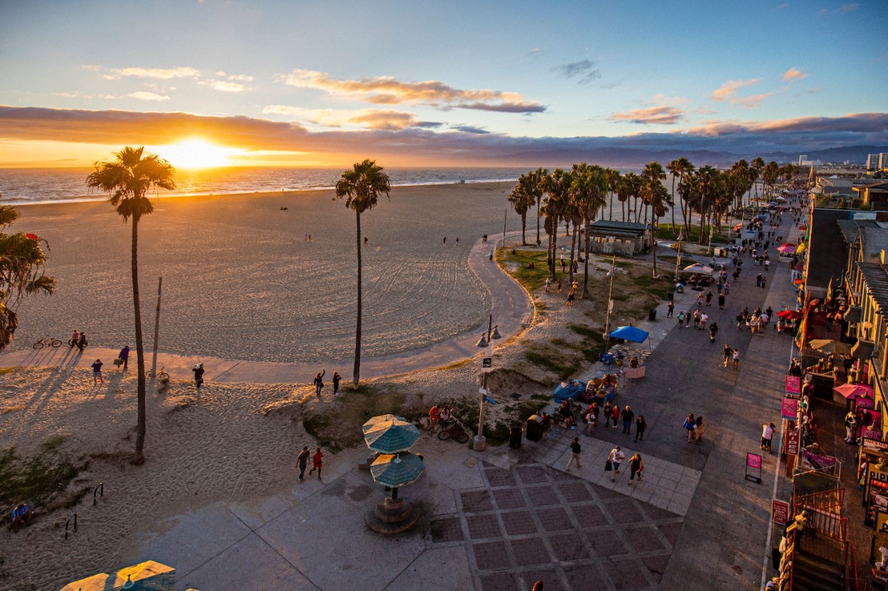 High angle view of Venice beach during sunset. Tourists are walking on footpath by ocean. Shot of beautiful nature and people is taken from above.